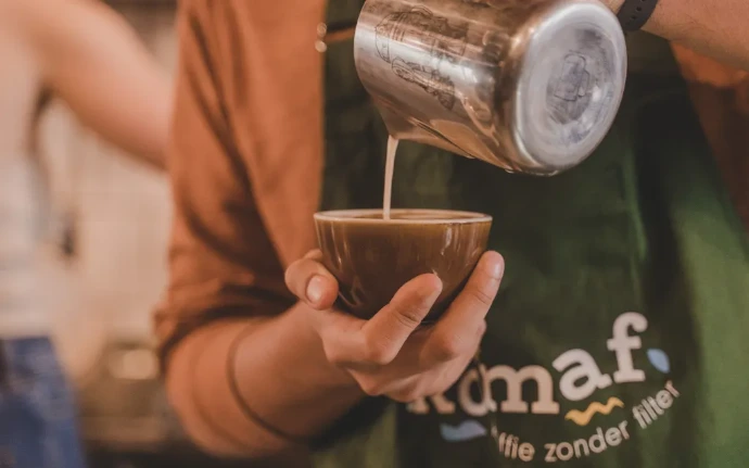 Een barista giet opgeschuimde melk in een tas koffie